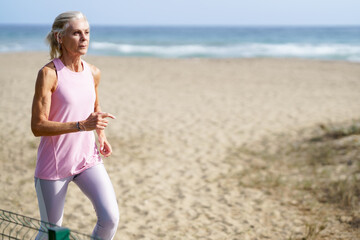 Mature woman running along the shore of the beach. Older female doing sport to keep fit