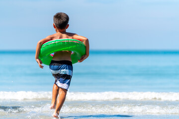 Little Asian boy in swimwear and swim ring playing in sea water on tropical beach in summer sunny day. Happy little child boy enjoy and fun outdoor activity lifestyle on travel vacation at the sea © CandyRetriever 