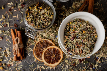 Herbal tea in a ceramic bowl and a glass jar on a black textural background. Detox and immunity tea. Herbal collection of chamomile, mint, lemon balm. rosehip and dried fruit pieces.