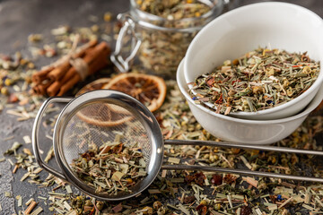 Fototapeta premium Herbal tea in a brewing strainer on a black textured background. Detox and tea for immunity. Herbal collection of chamomile, mint, lemon balm. pieces of wild rose and dried fruits.