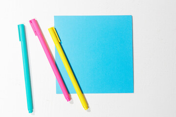 Multi-colored paper blue square on a white background, three multi-colored ballpoint pens. Office...