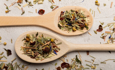 Fototapeta na wymiar Wooden spoons with herbal tea leaves on a light background. Top view. Detox and immunity tea. Herbal collection of chamomile, mint, lemon balm. rosehip and pieces of dried fruits.