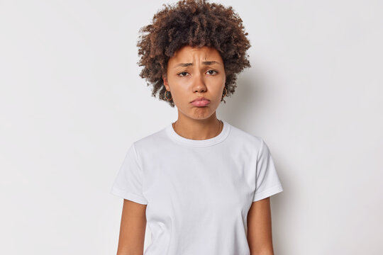Image of unhappy young woman with curly hair feels gross or pity grimaces displeased frowns upset dressed in casual t shirt isolated over white background thinks about something troublesome.