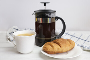 French-pressed ground coffee and a white porcelain cup and saucer. Preparing ground coffee in a press. Refreshing drink for breakfast.