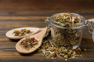 Dry herbal tea in a glass jar on a textured brown wood background. side view. Tea for detox and...
