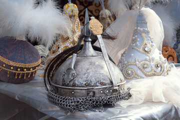 Metal helmet of a warrior against the background of delicate headdresses with feathers of Kazakh girls. Handmade