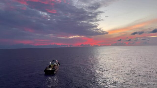 Supply vessel or crew boat with offshore oil and gas production platform in sun rise time with buetiful orange clouds and reflect of sun beam on the sea.