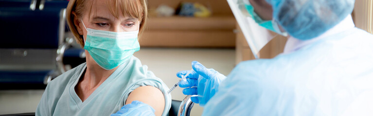 Doctor woman holding syringe and injection vaccine patient elderly in face mask for prevention...