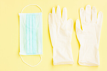 White latex protective gloves and green surgical mask on yellow background