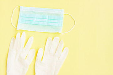 White latex protective gloves and green surgical mask on yellow background