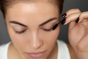 Mascara. Woman applying black mascara on eyelashes with makeup brush. Beautiful young woman face with natural eyebrows and eyelashes.