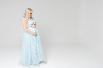 Fototapeta na wymiar Young pregnant woman, mom in a light dress, on a white background, indoors. Place for inscription 