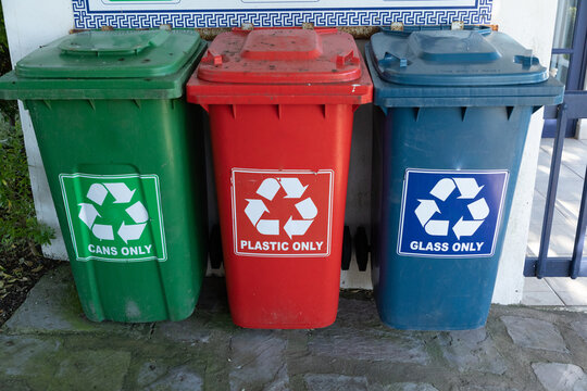 Three different coloured plastic bins for recycling. Green for cans red for plastic and a blue bin for glass. 