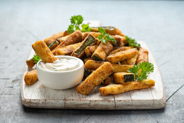 Crispy zucchini fries with sauce in white wooden board