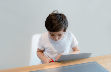 Naklejka premium Kid using scissors cutting cardboard , Schoolboy making art and craft for his homework,Child learning how to use the scissors cut the paper,Children learn and play at home, Home school concept