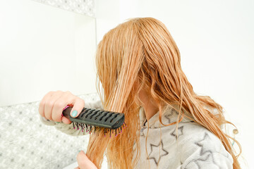 A woman combs her wet tangled hair after a bath. View from the back
