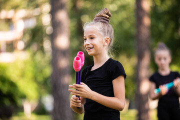 Portrait of joyful girl on rhythmic gymnastics training with clubs in summer in sports camp outdoors