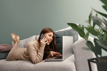 Beautiful woman speaking on mobile phone while using laptop for remote work. Online shoping