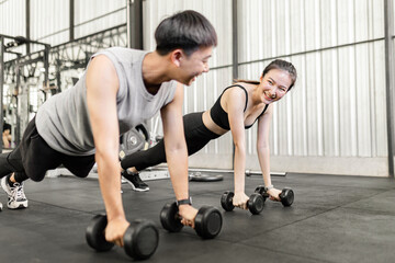 Fototapeta na wymiar exercise concept The female and male members of the gym doing the basic renegade row posture with dumbbells while looing at each other’s face