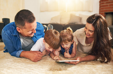 The tech savvy family is more connected than ever. Shot of an adorable brother and sister using a digital tablet with their parents on the floor at home.