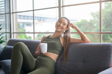 Young fitness woman in sportswear having a cup of coffee after exercising at home, Healthy and...