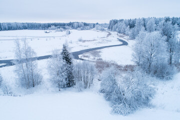 Aerial of a frosty and snowy rural landscape with a open river in Estonian winter, Northern Europe.	