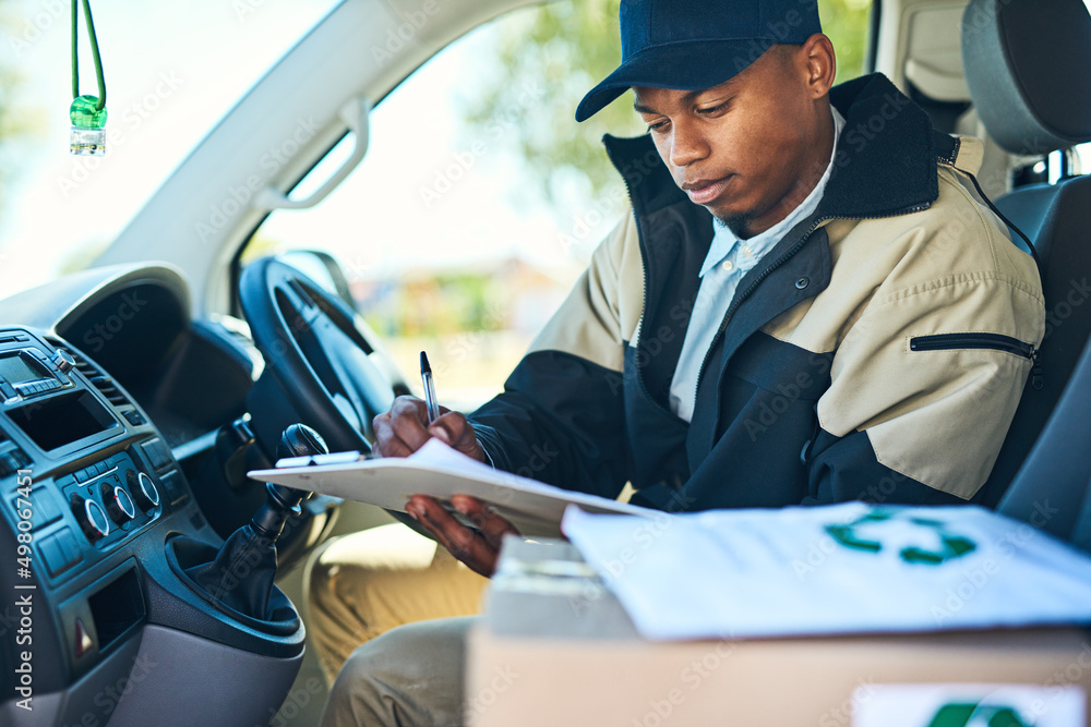 Poster Ive got just a few more stops to make. Shot of a courier writing on a clipboard while sitting in a delivery van.
