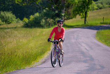Happy woman wearing bike helmet looking aside biking on a country road on a spring summer day.
