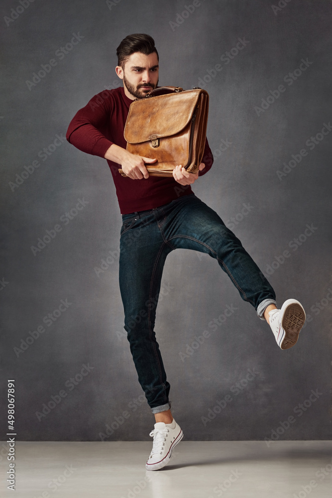 Poster kicking it up a notch. studio shot of a handsome young man posing with a bag against a dark backgrou