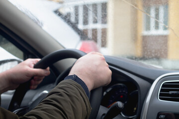 A man drives a car in rainy weather, a man's hands on the steering wheel of the car