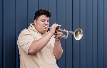 Young street musician playing the trumpet near the big blue wall