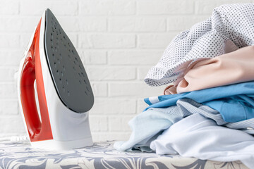Close-up of a stack of washed, rumpled clothes and a hot steam iron on an ironing board. The...