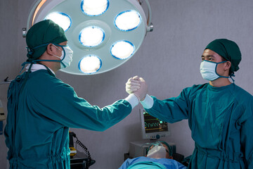 Portrait shot of doctor and assistance nurse wearing surgical coat while doing surgical operation for patient inside of the hospital. Medical and professional service occupation.