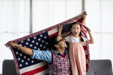 Father and daughter raise and holding American flag and celebrate United State independence date inside of the living room. Shoe feeling of happiness and joyful. Family holiday event.