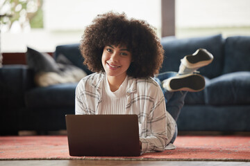 Blogging is a lifestyle. Shot of a young woman laying on the floor and using her laptop at home.