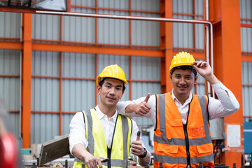 Selective focus at Asian men mechanical engineer, wearing safety equipment. While doing machine maintenance and safety control inside of factory area. With blurred background of heavy machine.