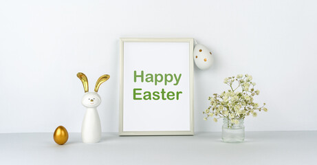 Happy Easter. Frame and flowers on background of white table and wall. Eggs and fun rabbit with golden ears. Decor