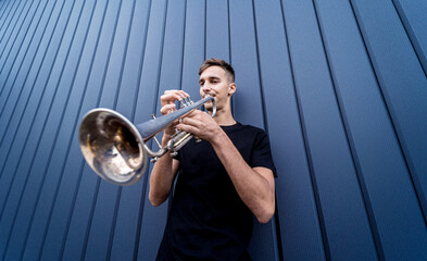 Young street musician playing the trumpet near the big blue wall