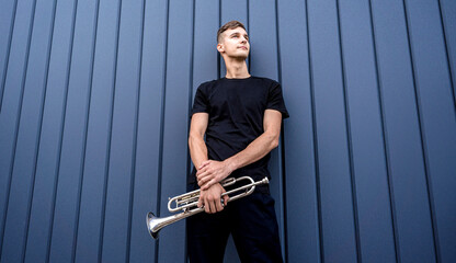 Young street musician playing the trumpet near the big blue wall © romaset