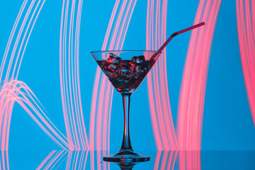A martini glass with ice cubes on a background of colored illumination.