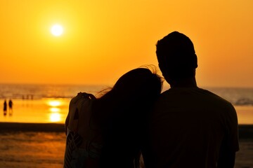 A beautiful silhouette of a couple enjoying their quality time at a beach during sunset. Love,...
