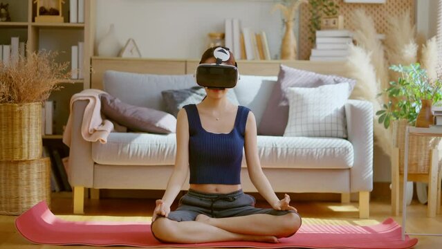 Peaceful clam asian female woman wearing virtual reality glasses meditating at home in breath train hands in namaste enjoying simulation and relax. Virtual  technology experience in metaverse world