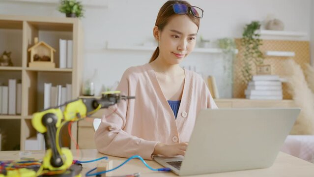 smart asian female programer learning robot arm ai coding electronic board cable in STEM, STEAM she try to testing her autonomous  robotic arm with sensors via Arduino platform at home