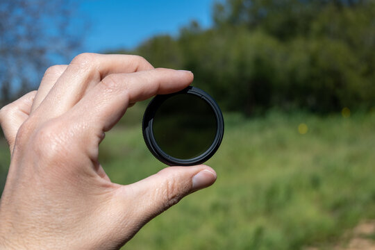 Close up of a  human hand holding an ND filter outdoors.