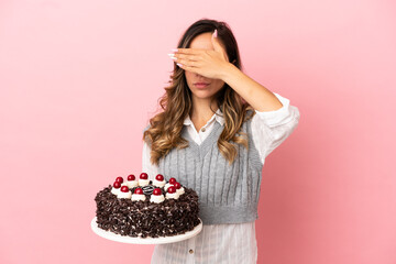 Young woman holding birthday cake over isolated pink background covering eyes by hands. Do not want to see something