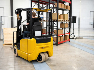 Man operates forklift. Forklift heading towards pallet rear view. Forklift next to storage racks. Special equipment for warehouse work. Warehouse worker career. Vehicle for moving goods