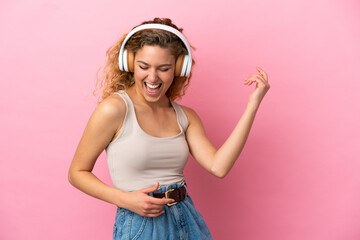 Young blonde woman isolated on pink background listening music and doing guitar gesture