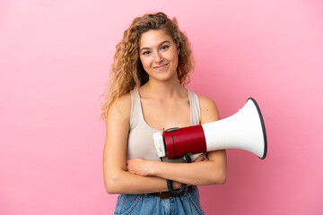 Young blonde woman isolated on pink background holding a megaphone and smiling