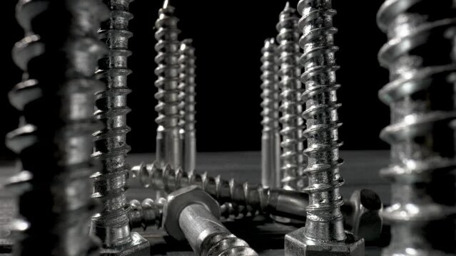 Screws, metal threaded bolts, fasteners on table on isolated black background. Steel chrome anchor screws in workshop or hardware shop. Super macro close up of fixing tools. Slow motion ready 59.97fps