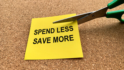 Scissors that cut yellow notepad with spend less save more text on wooden table background....